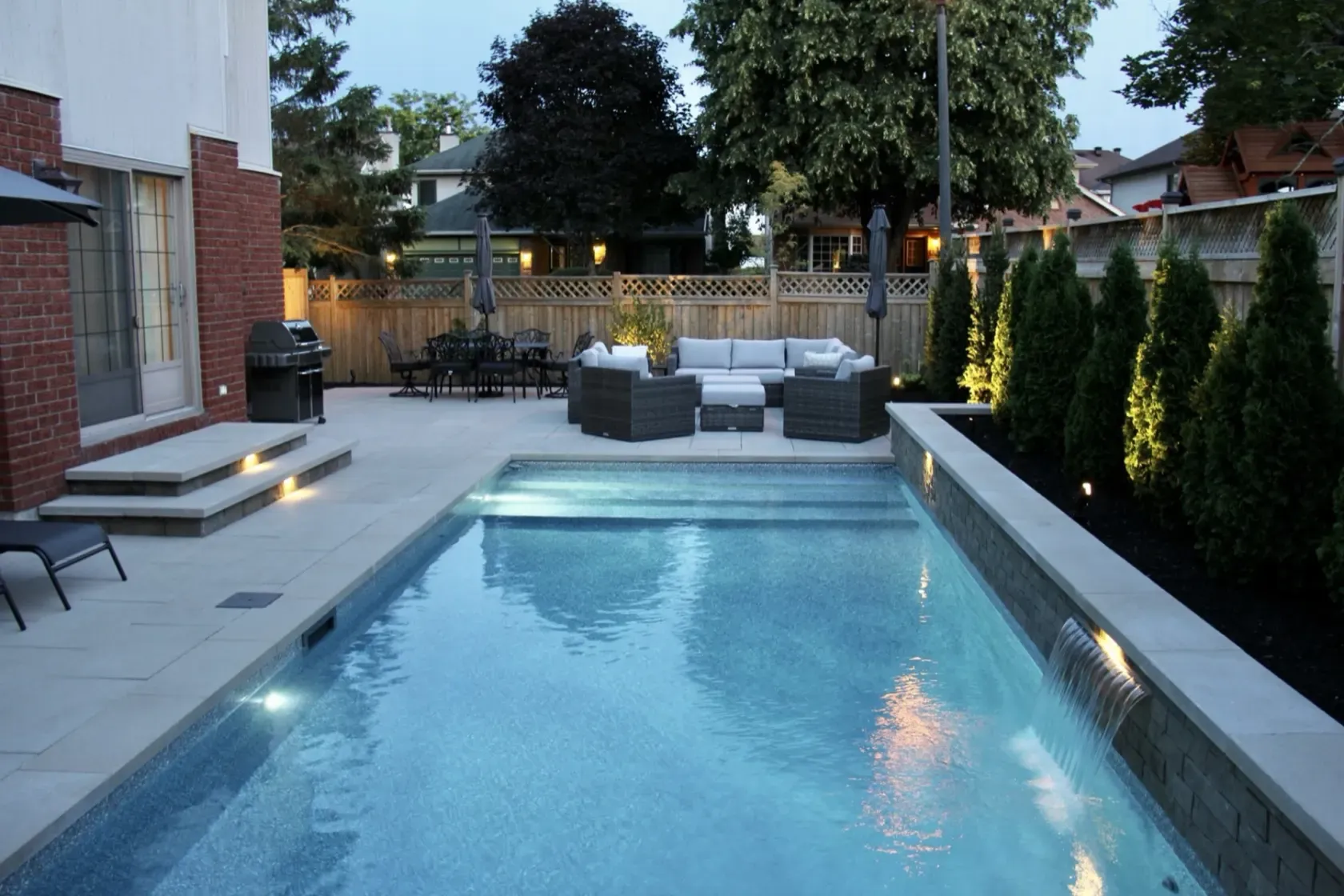 Inground pool at blue hour with the landscape and pool lights on and a sheer-descent waterfall