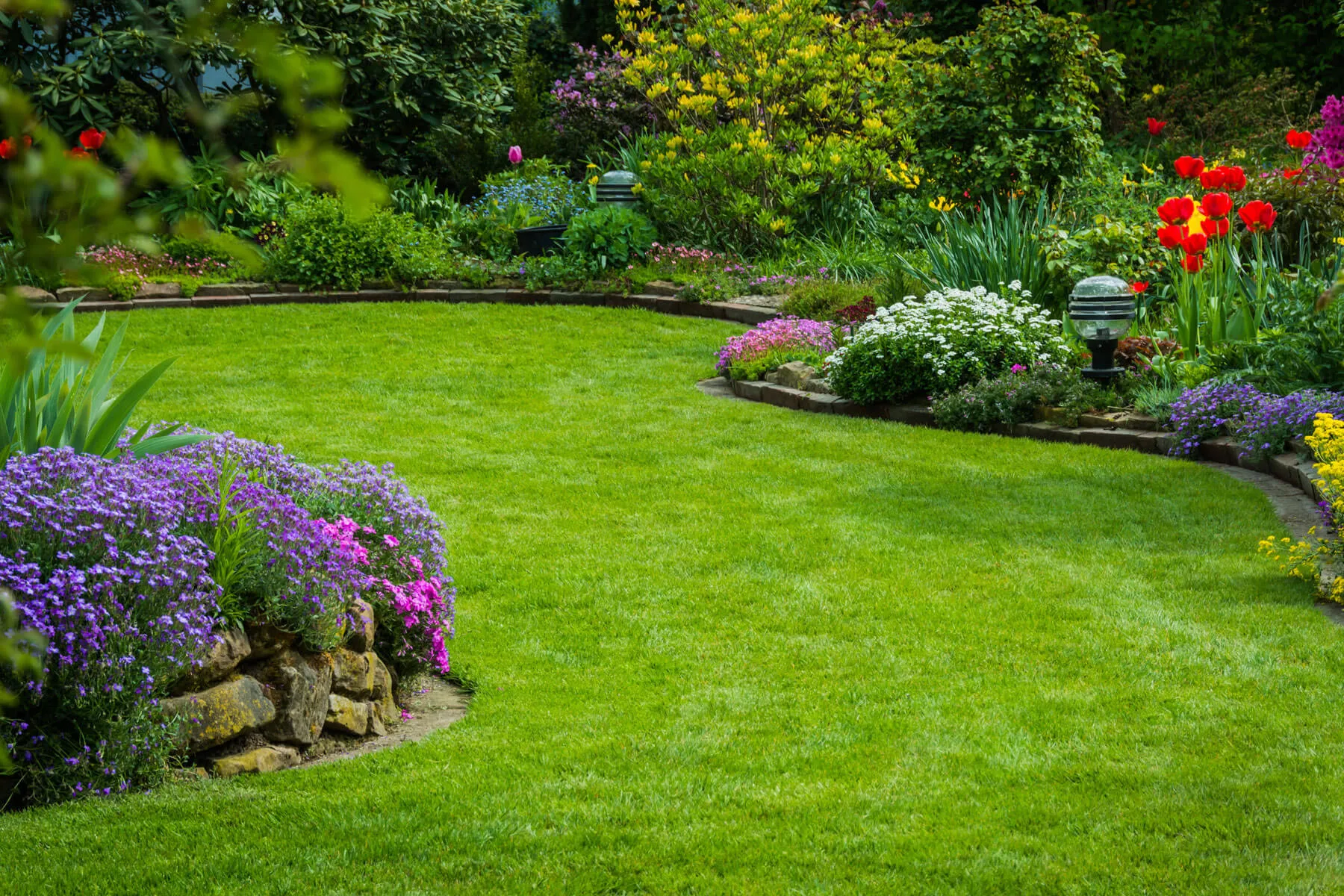 Layered flowering garden surrounding a maintained green lawn