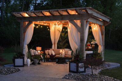 Backyard gazebo set up at night with lights and beautiful patio furniture on a manicured lawn